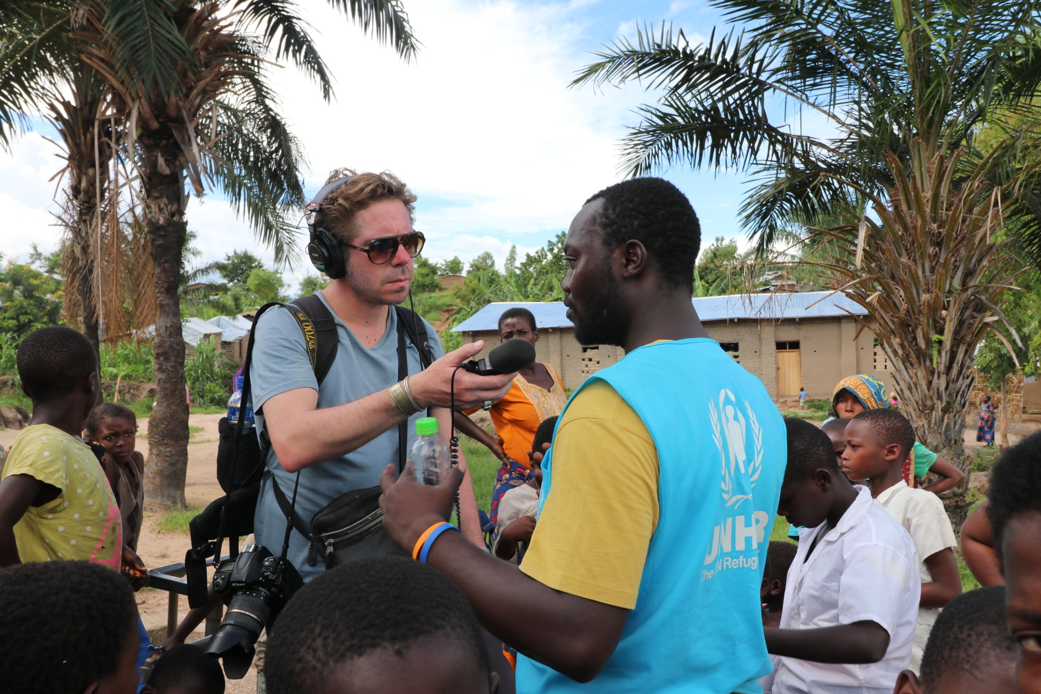 A journalist records an interview with a UNHCR colleague in the field
